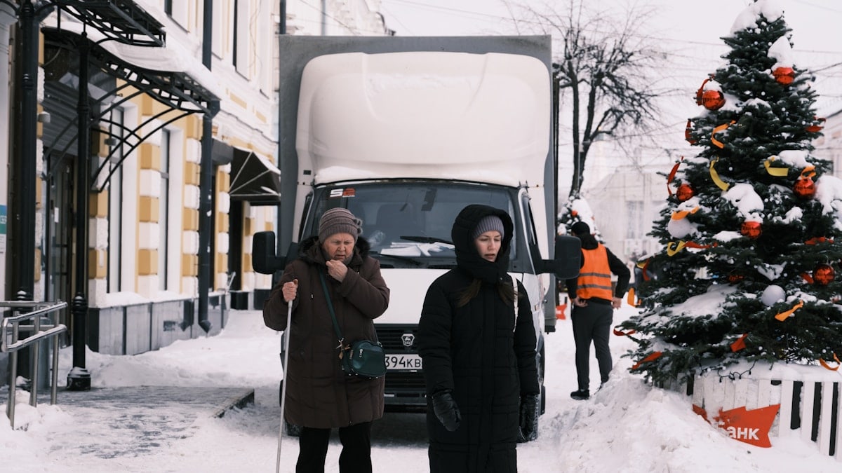 Two women walk on a snowy street near a truck